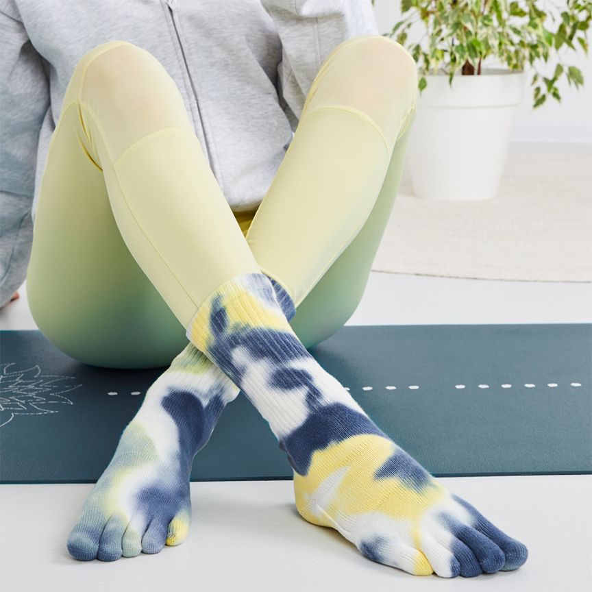 A person sitting with tie-dye five toe socks in yellow, blue, and gray colors, showing the five separate toe sections and the cushioned sole.