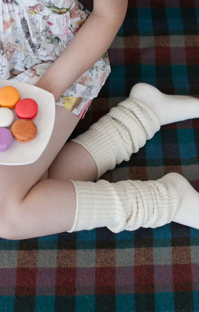 This is a picture of a woman relaxing while eating macaroons wearing Tabbisocks' product name Scrunchy Over The Knee Lounge Wool Blend Socks