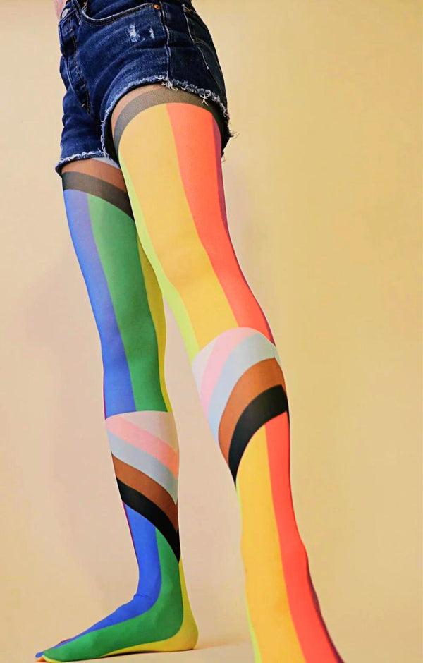 Lower half of a woman in short jeans wearing TABBISOCKS brand rainbow colored tights