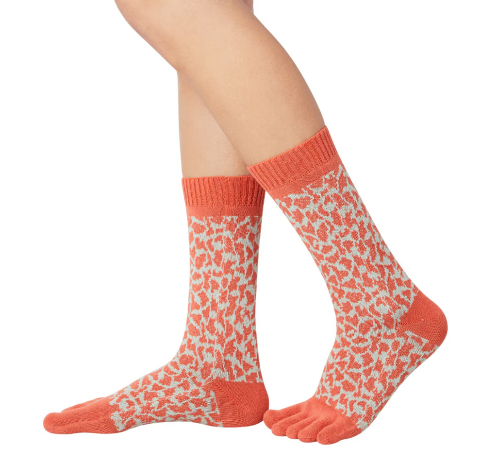 A pair of leopard print midcalf five toe socks worn on a person's feet, with the socks partially pulled down to show the toe separator design.