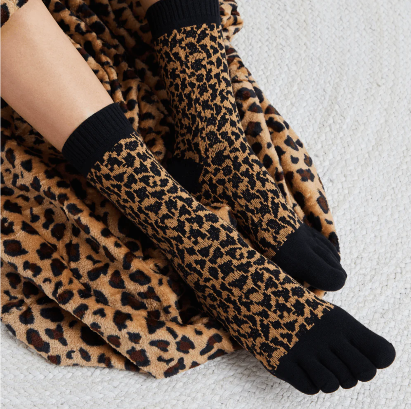 A pair of leopard print midcalf five toe socks worn on a person's feet, with the socks partially pulled down to show the toe separator design.