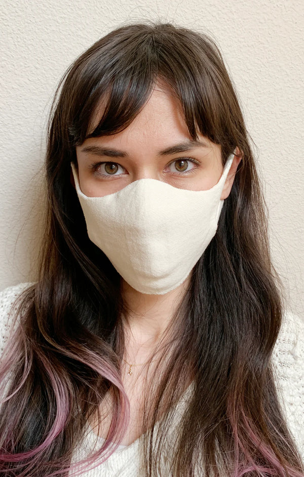 A woman with long hair wearing the Natural Ivory color of The Japanese Seamless Comfort Face Mask by Tabbisocks Wellness