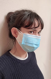 Side view of a woman in a black knit wearing a double layer of Tabbisocks Wellness Washable Silk Liner Face Mask and medical mask