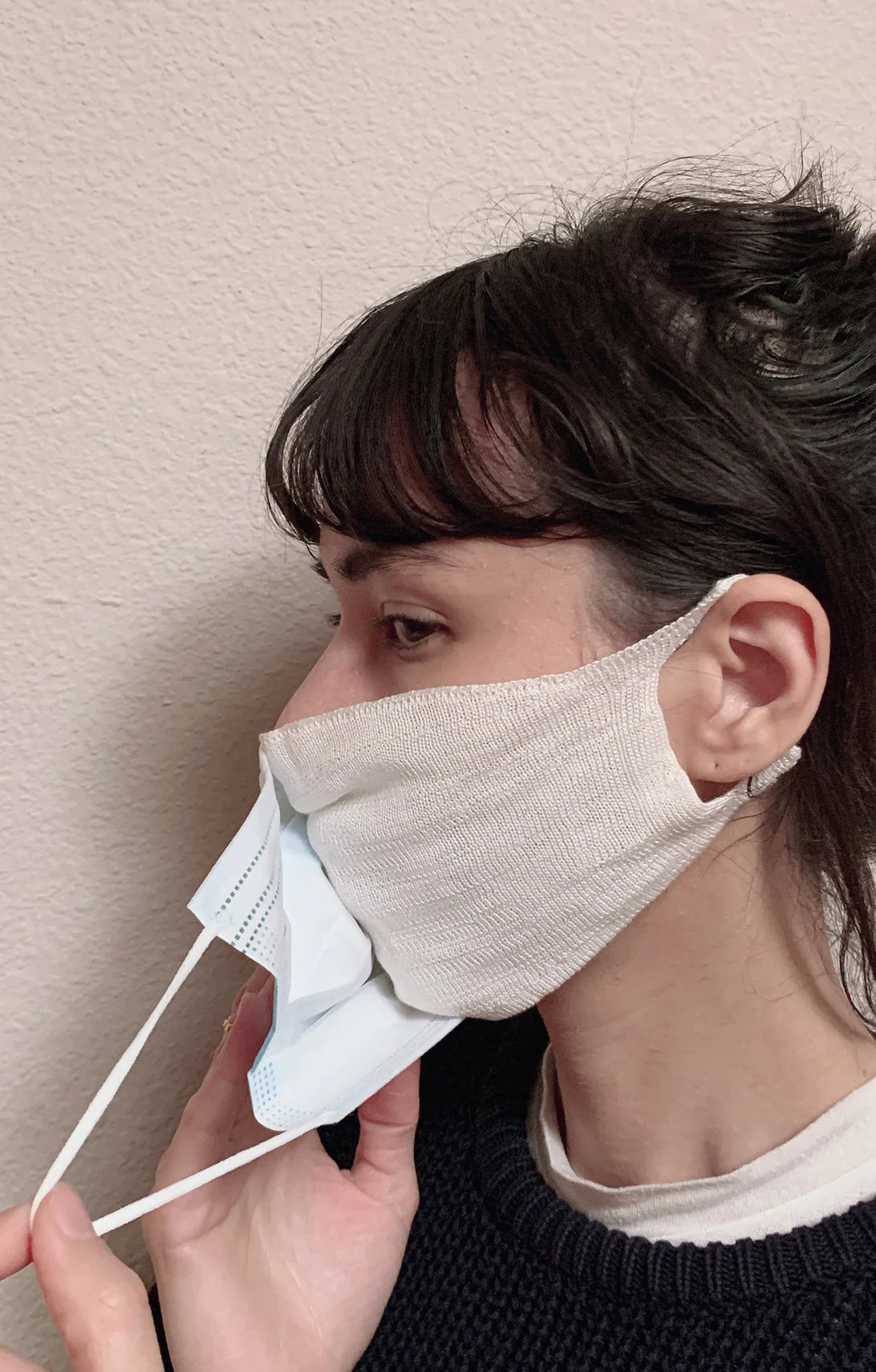 Side view of a woman in a black knit wearing a double layer of Tabbisocks Wellness Washable Silk Liner Face Mask and medical mask