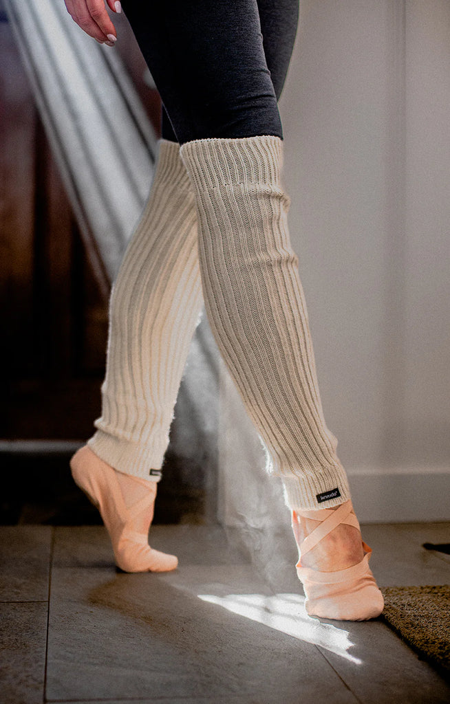 Lower half of a woman wearing ballet shoes and black spats wearing the Knitido plus brand Wool Blend Ribbed Leg Warmer in Ivory color