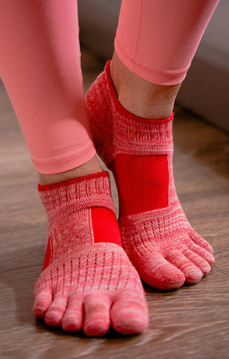 The feet of a woman wearing pinkish colored yoga pants wearing RED color with the product name Arch Support Grip Toe Socks With Power Pads by Knitido plus