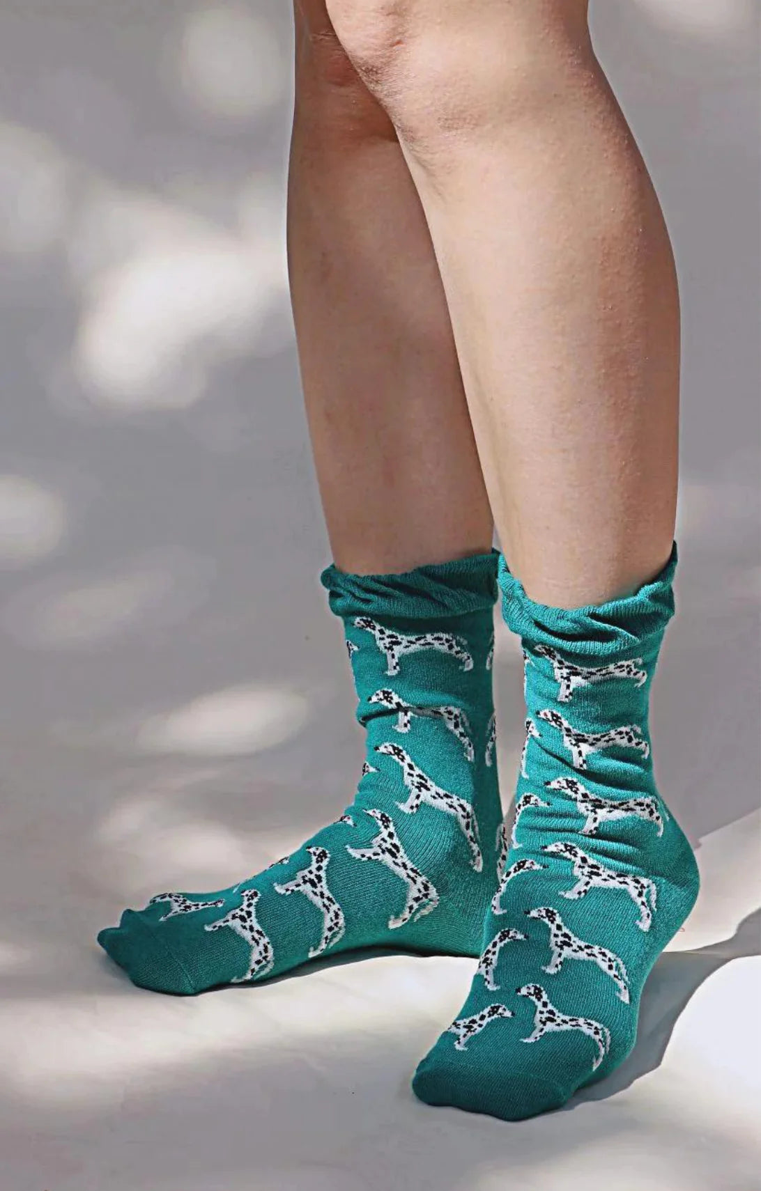 Tabbisocks brand's Animal Rescue Pairs DALMATIAN Socks, a pair of socks with emerald green fabric and a Dalmatian illustration scattered throughout, seen from a 45-degree angle on a woman's leg
