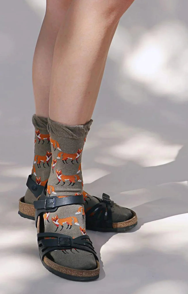 Tabbisocks brand Animal Rescue Pairs SCHNAUZER Dog Socks, a front view of a woman's leg wearing socks with an illustration of an orange fox on the entire sock in a gray/greenish fabric color