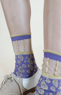 Socks with the trade name Golden Paisley Sheer Socks from Tabbisocks, on the feet of a woman wearing loafers in the AMETHYST color, a purplish color