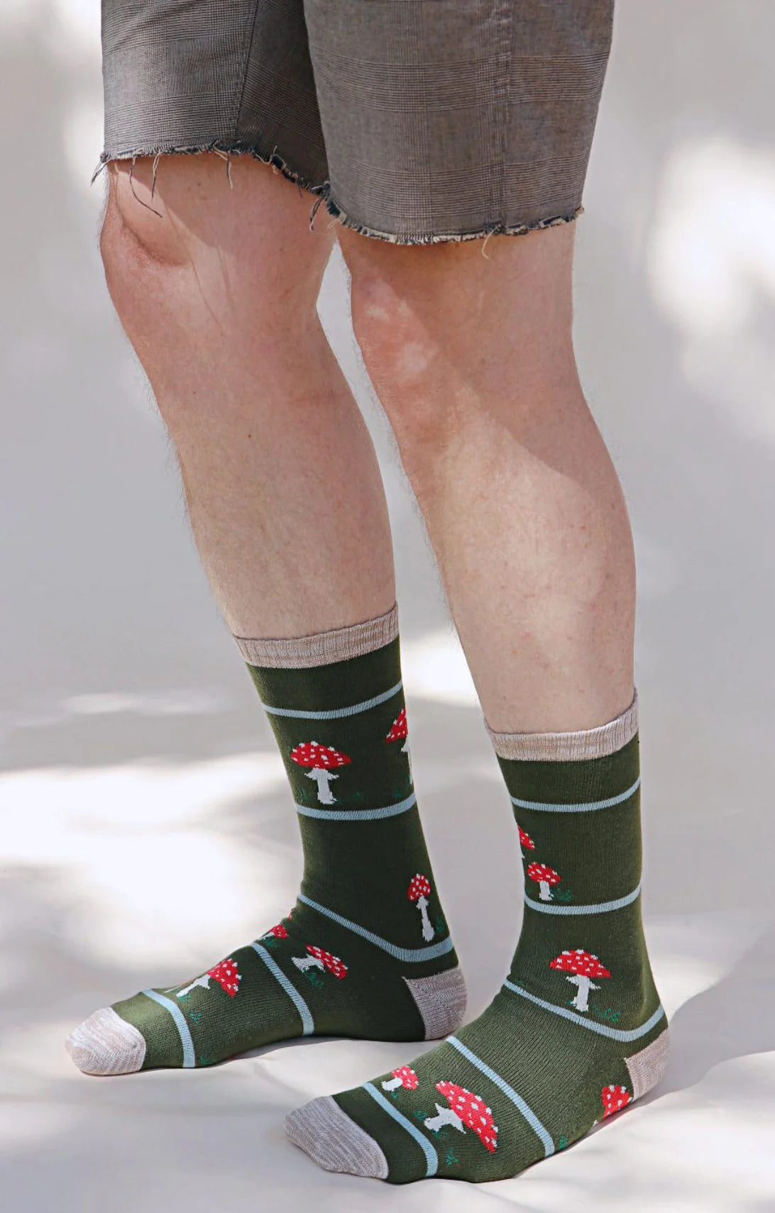 Lower half of a man wearing gray half pants with the product Replant Pairs Mushroom California Oregon Washington Organic Cotton Crew Socks by Tabbisocks in the color Green